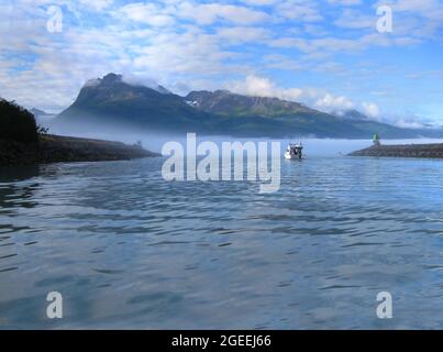 Fischerboot manuevers to open waters on the Bay of Valdez, Alaska. Am frühen Morgen steigt Nebel und Nebel aus dem Wasser auf und liegt über den Bergen. Stockfoto