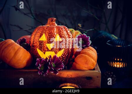 Dunkle Halloween Komposition mit Beleuchtung Jack-o-Laterne, dekorativen Kürbissen, Kerzen und Blumen. Halloween-Heimdekor. Selektiver Fokus. Stockfoto