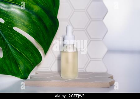 Mockup-Flasche mit natürlichem ätherischem Öl auf geometrischem Sechseck-Hintergrund mit grünem Monstera-Blatt auf weißem Hintergrund. Schönheits- und Körperpflegeprodukt. Hautpflege Stockfoto