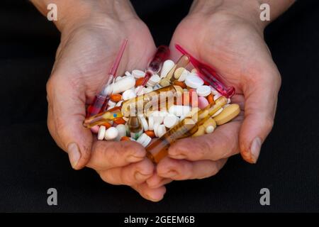 Eine Handvoll verschiedener Pillen in weiblichen Händen auf schwarzem Hintergrund Stockfoto
