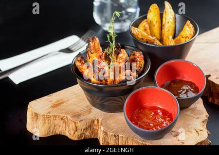 BBQ Hähnchenflügel mit Dip-Sauce und pommes frites. Nahaufnahme von Holztablett mit selektivem Fokus. Stockfoto