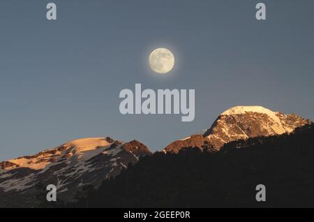 Vollmond in den Bergen. Der Mond erhellt die schneebedeckten Gipfel der Berge. Sonnenuntergang im Hochland. Stockfoto