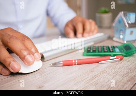 Nahaufnahme der Hände eines hispanischen Mannes, der in seinem Büro eine Computertastatur und -Maus verwendet Stockfoto