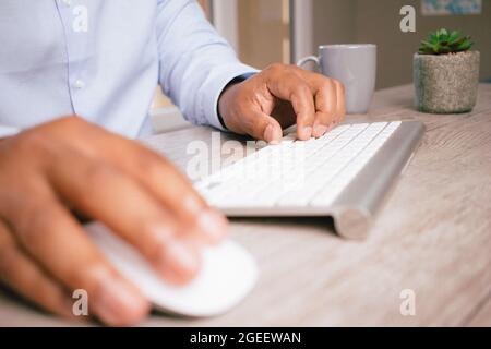 Nahaufnahme der Hände eines hispanischen Geschäftsmannes, der in seinem Büro eine Computermaus und eine Tastatur verwendet Stockfoto