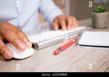Nahaufnahme der Hände eines hispanischen Mannes, der eine Computermaus verwendet und auf seiner Tastatur tippen kann Stockfoto