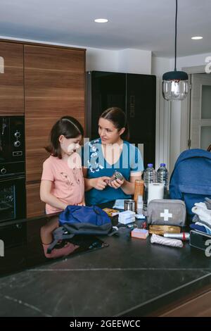 Mutter erklärt ihrer Tochter, wie sie einen Notfallrucksack vorbereiten soll Stockfoto