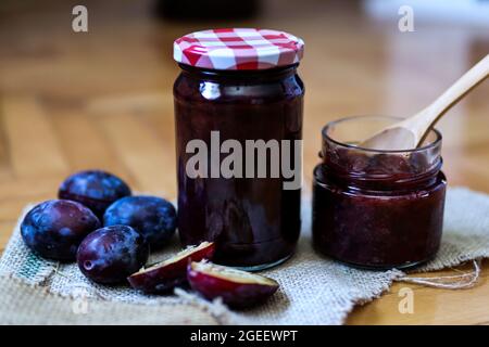 Pflaumenkonfitüre in Glasgläsern und frische Pflaumenfrüchte auf Retro-Hintergrund. Nahaufnahme, selektiver Fokus und Kopierbereich Stockfoto