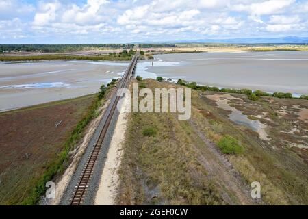 Drohnenflug entlang einer Eisenbahnlinie und in Richtung einer Brücke, die über einen Flutbach an der Küste führt. St. Lawrence, Queensland, Australien Stockfoto