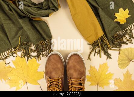 Orangefarbene Ledertasche, Schal, Herbstblätter auf beigem Hintergrund. Trendige Herbst-Accessoires. Gemütliches Outfit Stockfoto