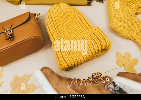 Orangefarbene Ledertasche, Strickpullover, Hut, Herbstblätter auf beigem Hintergrund. Trendige Herbst-Accessoires. Gemütliches Outfit Stockfoto