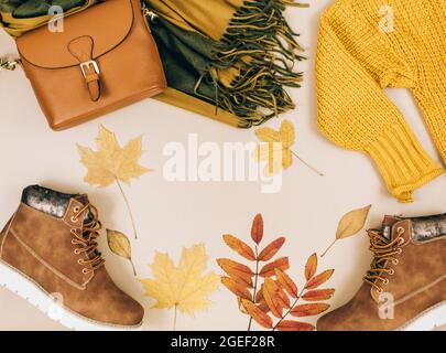 Orangefarbene Ledertasche, Strickpullover, Schal, Herbstblätter auf beigefarbenem braunen Hintergrund. Trendige Herbst-Accessoires. Gemütliches Outfit Stockfoto