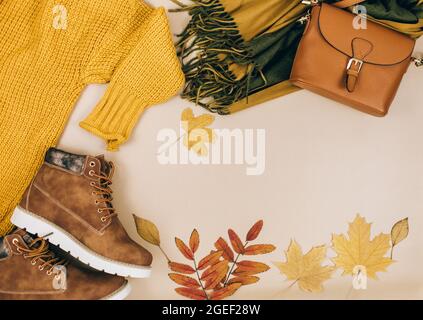 Orangefarbene Ledertasche, Strickpullover, Schal, Herbstblätter auf beigefarbenem braunen Hintergrund. Trendige Herbst-Accessoires. Gemütliches Outfit Stockfoto