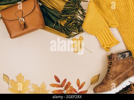 Orangefarbene Ledertasche, Strickpullover, Schal, Herbstblätter auf beigefarbenem braunen Hintergrund. Trendige Herbst-Accessoires. Gemütliches Outfit Stockfoto