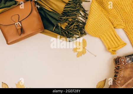 Orangefarbene Ledertasche, Strickpullover, Schal, Herbstblätter auf beigefarbenem braunen Hintergrund. Trendige Herbst-Accessoires. Gemütliches Outfit Stockfoto