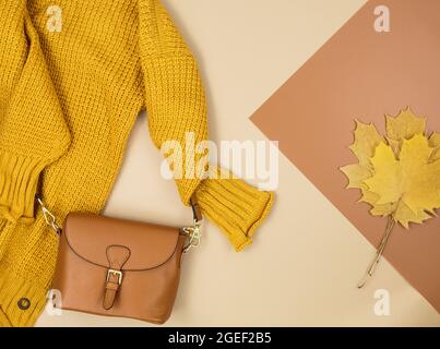 Orangefarbene Ledertasche, braune Schuhe, Schal, Herbstblätter auf grauem Hintergrund. Trendige Herbst-Accessoires. Gemütliches Outfit Stockfoto