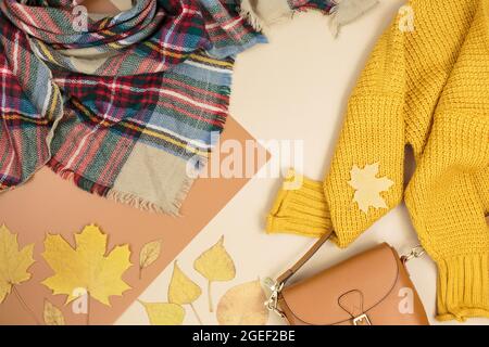 Orangefarbene Ledertasche, Strickpullover, Schal, Herbstblätter auf beigefarbenem braunen Hintergrund. Trendige Herbst-Accessoires. Gemütliches Outfit Stockfoto