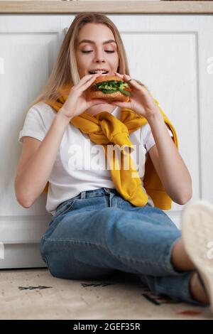 Junge Frau, die in der Küche leckeren veganen Burger isst Stockfoto