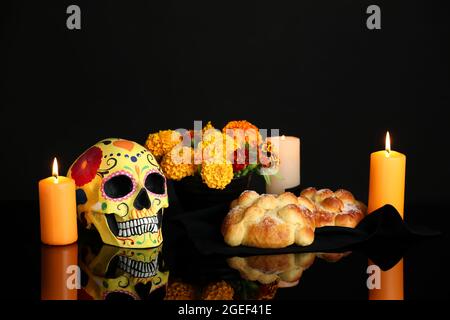 Brot der Toten und bemalter Schädel auf dunklem Hintergrund. Feier des mexikanischen Tages der Toten (El Dia de Muertos) Stockfoto