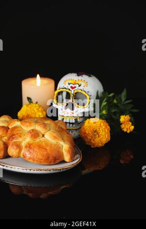 Brot der Toten und bemalter Schädel auf dunklem Hintergrund. Feier des mexikanischen Tages der Toten (El Dia de Muertos) Stockfoto