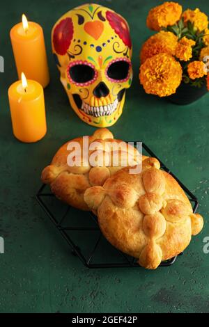 Brot der Toten und bemalter Schädel auf farbigem Hintergrund. Feier des mexikanischen Tages der Toten (El Dia de Muertos) Stockfoto