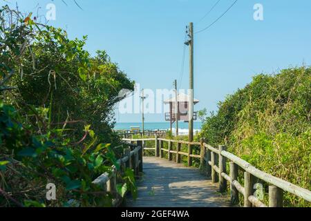 Florianopolis, Brasilien. 10. August 2019: Holzpromenade am Strand mit Rettungsschwimmerturm an einem leeren Strand mit klarem Sand und blauem Meer im Süden Stockfoto