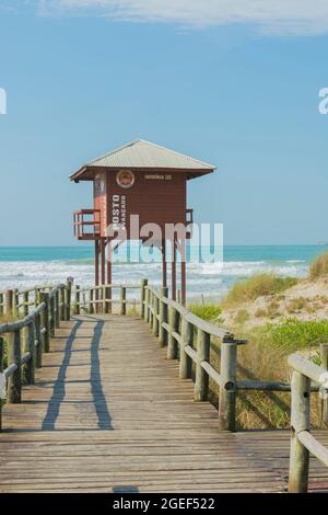 Florianopolis, Brasilien. 10. August 2019: Holzpromenade am Strand mit Rettungsschwimmerturm an einem leeren Strand mit klarem Sand und blauem Meer im Süden Stockfoto