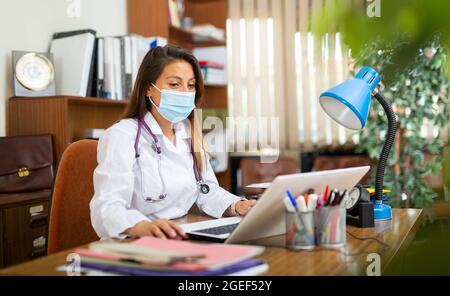 Hispanische Frau Arzt in Gesichtsmaske sitzt im Büro Stockfoto