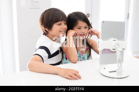 Zwei Birazialkinder, die während der covid Lockdown zu Hause eine virtuelle Online-Schulbildung besuchen, lächeln Stockfoto