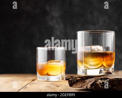 Zwei Gläser mit Eiswürfel und Whiskey auf einem alten Holztisch. Speicherplatz kopieren. Stockfoto