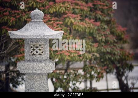 Flacher Fokus einer weiß verzierten Säule mit grün roten Blättern im Hintergrund im Park, Japan Stockfoto