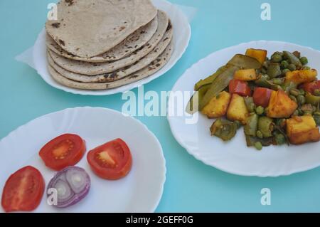 Indian Food - Matar Paneer Gemüse, Roti und Salat auf weißem Teller mit hellblauem Hintergrund Stockfoto