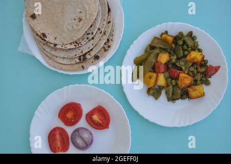 Indian Food - Matar Paneer Gemüse, Roti und Salat auf weißem Teller mit hellblauem Hintergrund Stockfoto