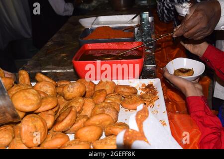 Hand eines indischen Mannes, der Chutney in Kachori in seinem Teller mit einem Löffel aus einem großen Topf trug Stockfoto