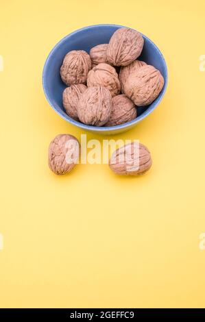 Vertikale Aufnahme von ganzen Walnüssen in einer kleinen Schüssel mit zwei Walnüssen isoliert auf einem gelben Hintergrund Stockfoto