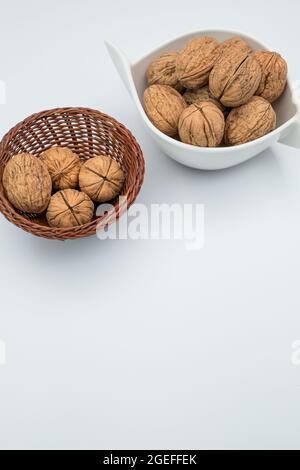 Vertikale Aufnahme von ganzen Walnüssen in einem kleinen Korb und einer weißen Schale isoliert auf weißem Hintergrund Stockfoto