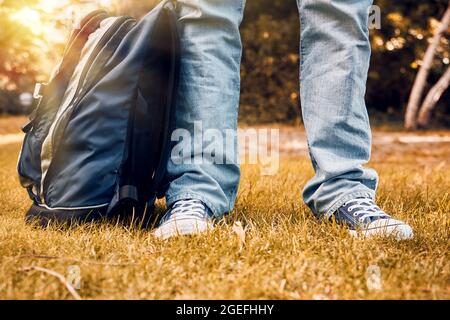 Junge Teenager Fuß und Beine mit Sneakers, Jeans und einem Rucksack auf herbstlichem Gartengras. Zurück zum Schulkonzept. Stockfoto