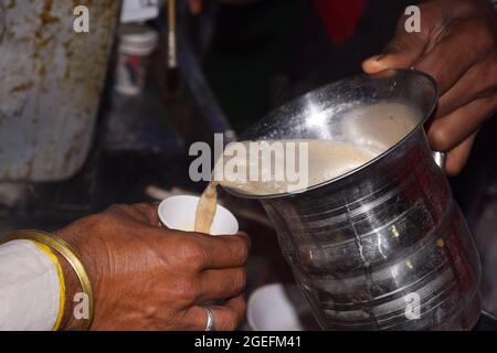 Man's Hand gießt Tee in die Tasse mit Edelstahl-Becher Stockfoto