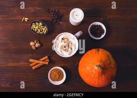 Kürbis-Gewürz-Latte-Becher unter natürlichen Gewürzen von Zimt, Kardamom, Nelken und Muskatnuss auf dunkelbraunem Holztisch, flach liegend Stockfoto