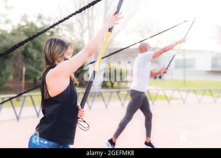 Seitenansicht des Fitnesspaares, das mit einem Fitnessband im Park trainiert. Stockfoto