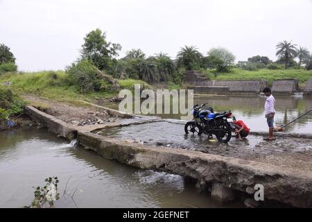 Ländliche Kinder waschen Fahrräder mit Flusswasser, natürliches Grün im Hintergrund Stockfoto