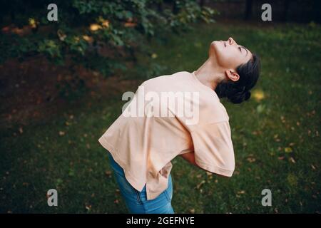 Sportliche Millennial Indian Woman in Freizeitkleidung Stretching vor dem Training im Park, beim Aufwärmen von Rückenübungen. Stockfoto