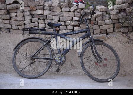 Altes schwarz gefärbtes Fahrrad von Kindern, die auf der Wand ruhen, Konzept des indischen Dorfes Stockfoto