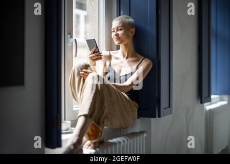 Stilvolle Frau, die am Fenster telefoniert Stockfoto
