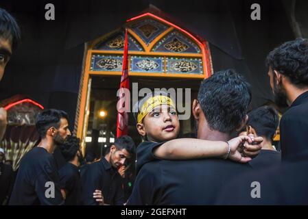 Ein schiitischer Junge aus Kashmiri schaut während der Ashura-Prozession in Srinagar zu. Schiitisch-muslimische Gläubige beten, schlagen ihre Brust, singen religiöse Slogans und verteilen religiöse Speisen namens „nazri“, während sie Aspekte der Tötung von Imam Hussain und seinen 72 Anhängern im Jahr 680 n. Chr. in Karbala auf Aschura (dem 10. Von Muharram) im heutigen Irak nachspielen, Durch die viel größeren Armeen der Yeziden. Imam Hussain wird unter den Schiiten als der „Herr der Märtyrer“ verehrt, dessen Widerstand und Bereitschaft, angesichts überwältigender Gewalt für seinen religiösen Glauben zu sterben, von Shias als Vorbild für dai verehrt wird Stockfoto