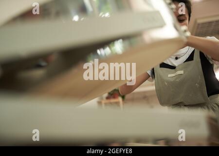 Niedriger Winkel der jungen erfahrenen weiblichen Meister in Schürze öffnen Heizkammer für das Backen von Ton während der Arbeit in Keramik-Kunst-Studio Stockfoto