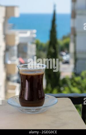 Türkischer Kaffee in transparentem, traditionellem Glas an Gebäuden und Blick auf das Meer mit Bäumen im Sommer Stockfoto