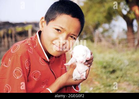 Indisches ländliches Kind in glücklicher Haltung, trägt rotes Hemd, mit Hund Welpen Stockfoto