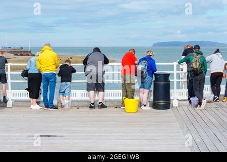 Touristen und Besucher genießen einen Sommernachmittag beim Angeln nach Krabben am Beaumaris Pier Anglesey North Wales Stockfoto