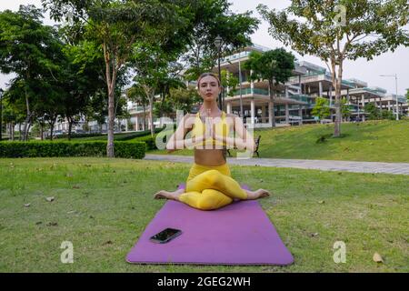 Yoga Übung - Frau tut Yoga Pose Meditation im öffentlichen Park Sport, gesundes Konzept. Gelbe Sportbekleidung Stockfoto