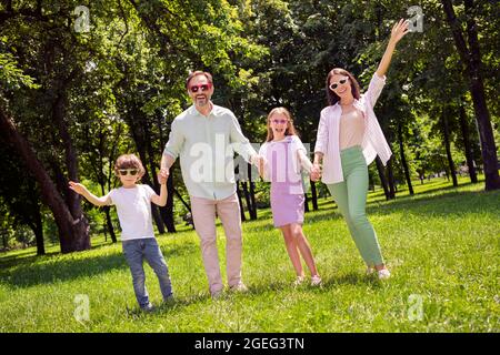 Foto von funky niedlich preteen junge Mädchen Mutter Vater gekleidet casual Outfit steigt Arme mit Spaß zu Fuß lächelnd außerhalb Stadtpark Stockfoto